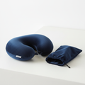 Memory foam travel neck pillow in dark navy velvet, U-shaped, folded next to its carry pouch on a white surface