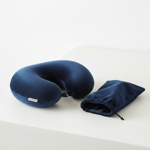 Memory foam travel neck pillow in dark navy velvet, U-shaped, folded next to its carry pouch on a white surface